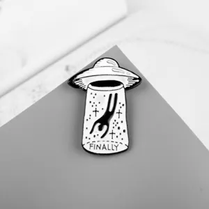 Detail view of black and white UFO alien abduction enamel pin with FINALLY inscription.