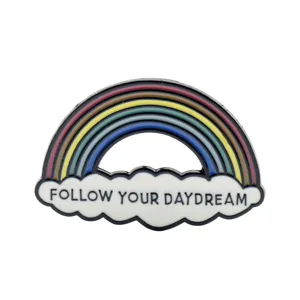Primo piano di una spilla in smalto arcobaleno con la scritta 'Follow Your Daydream' su nuvola