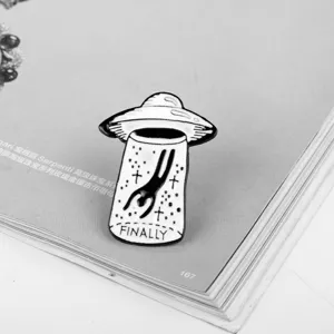 Close-up detail of a creative black and white UFO enamel pin badge with Finally text