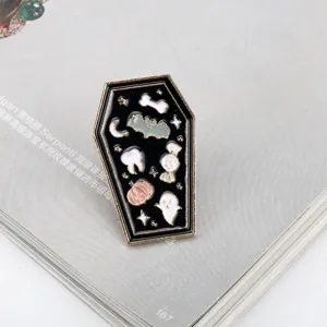 Close-up of a Halloween cartoon coffin-shaped enamel pin featuring ghost, bat, and pumpkin motifs