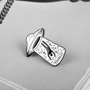 Detailed macro view of a creative black and white UFO enamel pin with alien and finally text