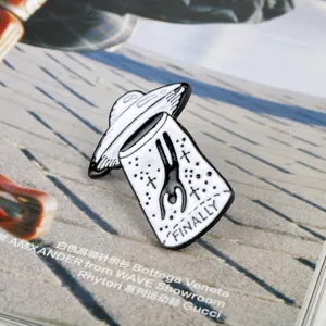 Macro view of a creative black and white UFO abduction enamel pin with FINALLY text.