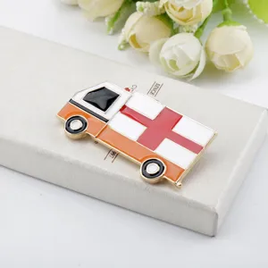 Dettaglio di una spilla smaltata a forma di ambulanza con croce rossa su scatola regalo