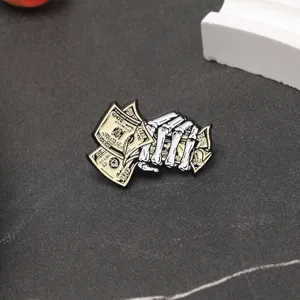 Détail d'un pin's émaillé représentant une main de squelette tenant de l'argent.