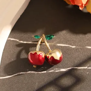 Gros plan détaillé d'une broche cerise rouge avec des feuilles en cristal vert facetté.