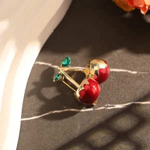 Gros plan détaillé d'une broche cerise en émail rouge avec des cristaux verts.