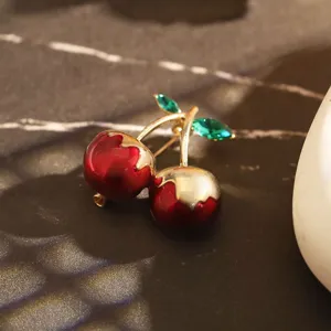 Détail d'une broche cerise élégante avec émail rouge brillant et cristaux verts