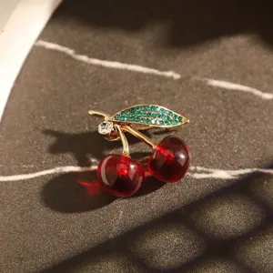 Vue rapprochée de la broche cerise avec des fruits rouges et une feuille de strass verts
