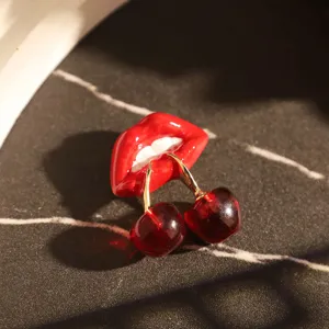 Détail d'une broche créative de lèvres rouges et cerises sur un fond de pierre noire.