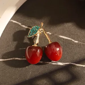 Gros plan détaillé d'une broche cerise avec fruits rouges et strass verts brillants