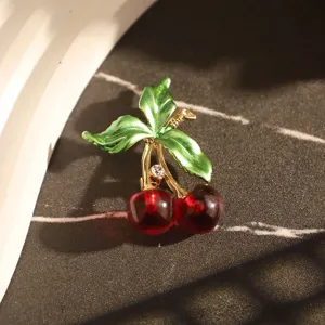Vue détaillée d'une broche cerise créative avec feuilles en émail vert et perles rouges.