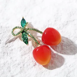 Gros plan d'une élégante broche cerise avec feuilles en strass verts et fruits rouges.