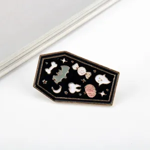 Macro detail shot of a black coffin-shaped Halloween enamel pin with cartoon icons.