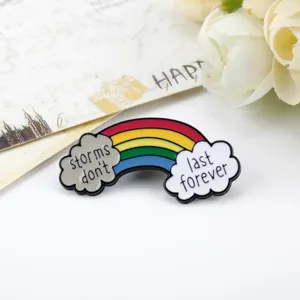 Primo piano di una spilla smaltata arcobaleno con citazione storms don't last forever