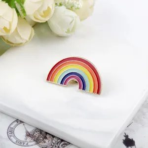 Dettaglio di una spilla smaltata arcobaleno vibrante esposta su una base di marmo bianco