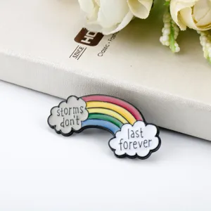 Dettaglio di una spilla in smalto arcobaleno con nuvole e scritte