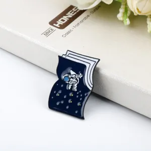 Macro view of an astronaut space enamel pin badge in a book shape on a gift box.