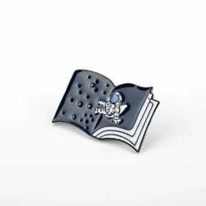 Detailed close-up of a cartoon astronaut book enamel pin featuring starry space design