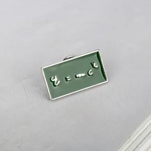 Macro detail view of a green rectangular enamel pin with E=mc² physics formula design.