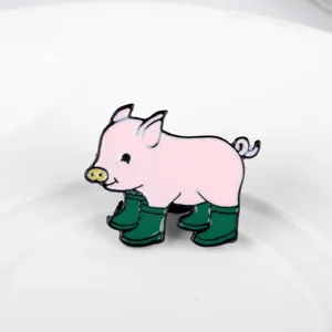 Close-up detail showing a cute pink pig wearing green rain boots enamel pin brooch accessory