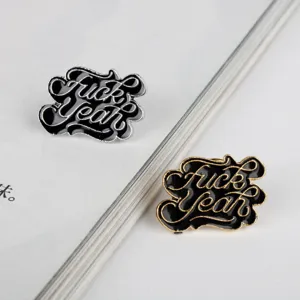 Detailansicht von schwarzen Emaille-Pins mit 'Fuck Yeah'-Schriftzug in Gold und Silber.