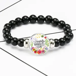 Close-up detail of a stretch bracelet featuring a glass gem with floral art and quote