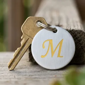 Vue détaillée d'une breloque ronde en métal avec une lettre M cursive dorée.