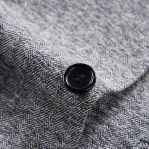 Detailed macro view of gray herringbone wool-like suit fabric featuring a black button