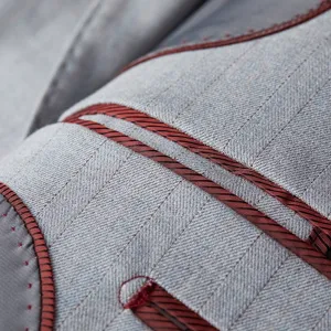 Detailed view of light gray men's suit fabric with burgundy piping and stitching