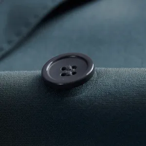 Close-up detail of a dark button on a teal men's slim fit business suit jacket fabric