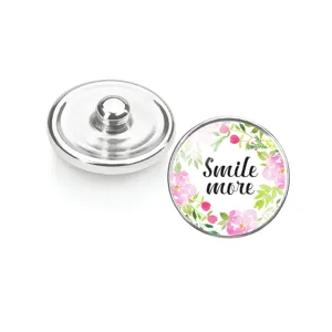Détail d'un bouton pression en verre fleuri avec le texte 'Smile more' et base métal.