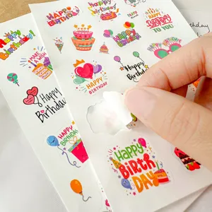 Gros plan d'une main décollant un autocollant d'anniversaire coloré d'une feuille