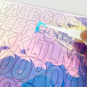 Holographic 1-inch alphabet stickers being peeled with tweezers for DIY projects