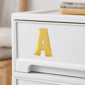 Gros plan d'un grand autocollant lettre A en or brillant sur un tiroir blanc pur.