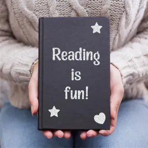 Glitter silver letter stickers forming 'Reading is fun!' on a black notebook cover