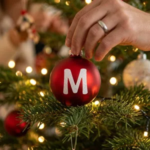Close-up of a sparkling glitter letter M sticker on a red Christmas tree ball ornament