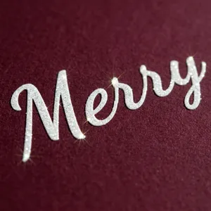 Macro view of white glitter "Merry" script sticker on burgundy textured background