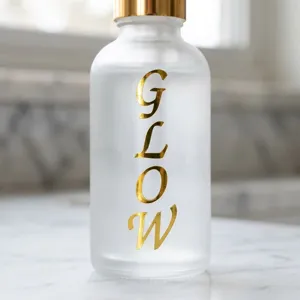 Detaillierte Nahaufnahme eines goldfarbenen 1-Zoll-GLOW-Alphabet-Aufklebers auf einer Glasflasche