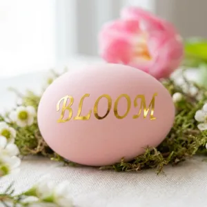 Nahaufnahme eines goldfarbenen BLOOM-Buchstabenaufklebers auf einem rosa Osterei.