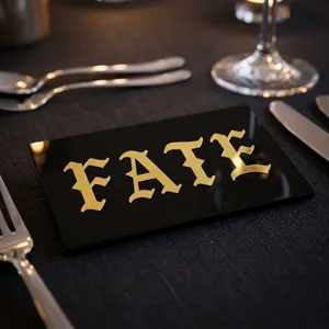 Makrodetail der goldenen gotischen Alphabet-Aufkleber mit dem Wort FATE auf schwarzer Platte