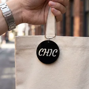 Close-up of a circular black mirror acrylic tag with silver CHIC lettering on a canvas bag