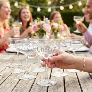 Nahaufnahme des silbernen 'Cheers' Aufklebers auf einem Sektglas bei einer Gartenparty