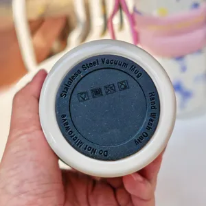 Bottom detail view of stainless steel vacuum mug showing care instructions and icons.