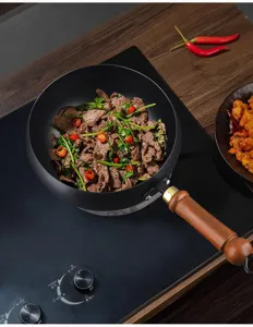Detail van de handgesmede zwarte ijzeren wok met houten handvat op inductiekookplaat