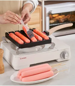 Action shot of the non-stick sausage grilling pan being used on a stove with a silicone brush.