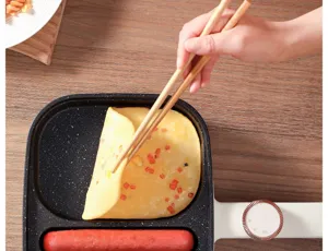 Détail d'une poêle à petit-déjeuner électrique 3-en-1 retournant une omelette avec des baguettes