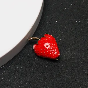 Detailed view of red strawberry charm, glossy metal enamel brooch pendant, close-up product shot.