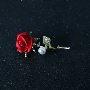 Close-up of a stylish red rose brooch with sparkling rhinestones, gold stem and a white pearl accent.