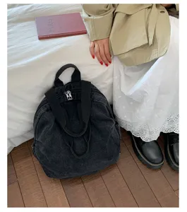 Vue détaillée d'un sac à dos en denim noir lavé rétro sur sol en bois dans un décor.