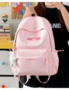 Detalle frontal de mochila de lona rosa, patrón de letras bordadas y bonito colgante de estrella.